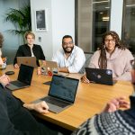 Diverses Team sitzt konzentriert in einer Besprechung am Tisch mit Laptops