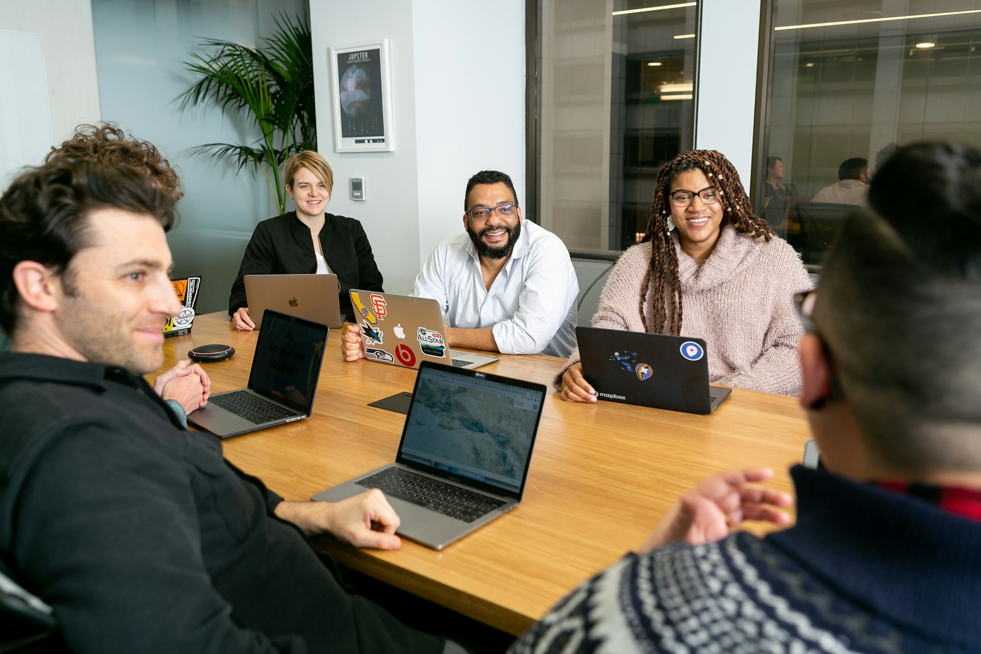 Diverses Team sitzt konzentriert in einer Besprechung am Tisch mit Laptops